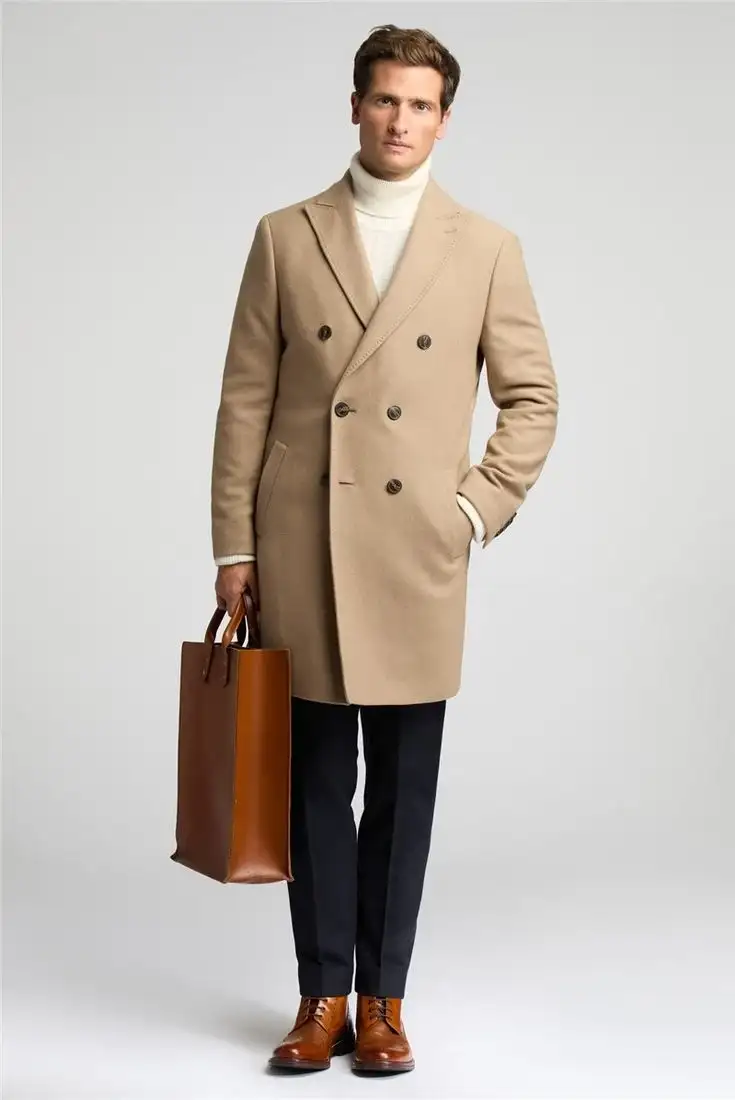 Camel-colored double-breasted men's overcoat layered over cream turtleneck sweater with dark trousers and tan boots, carrying a brown leather tote – Nordic Bespoke Tailor winter fashion
