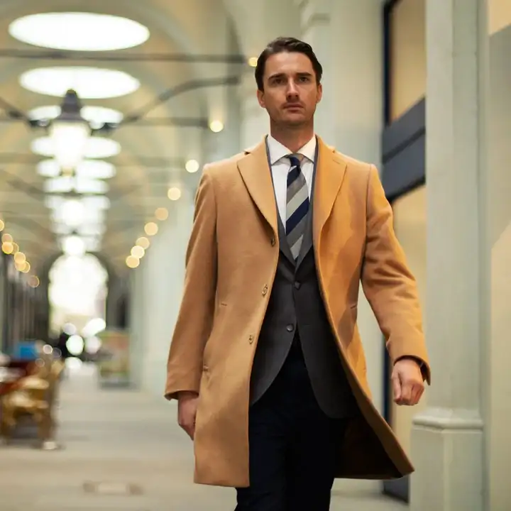 Male model wearing camel overcoat layered over suit for winter tailoring