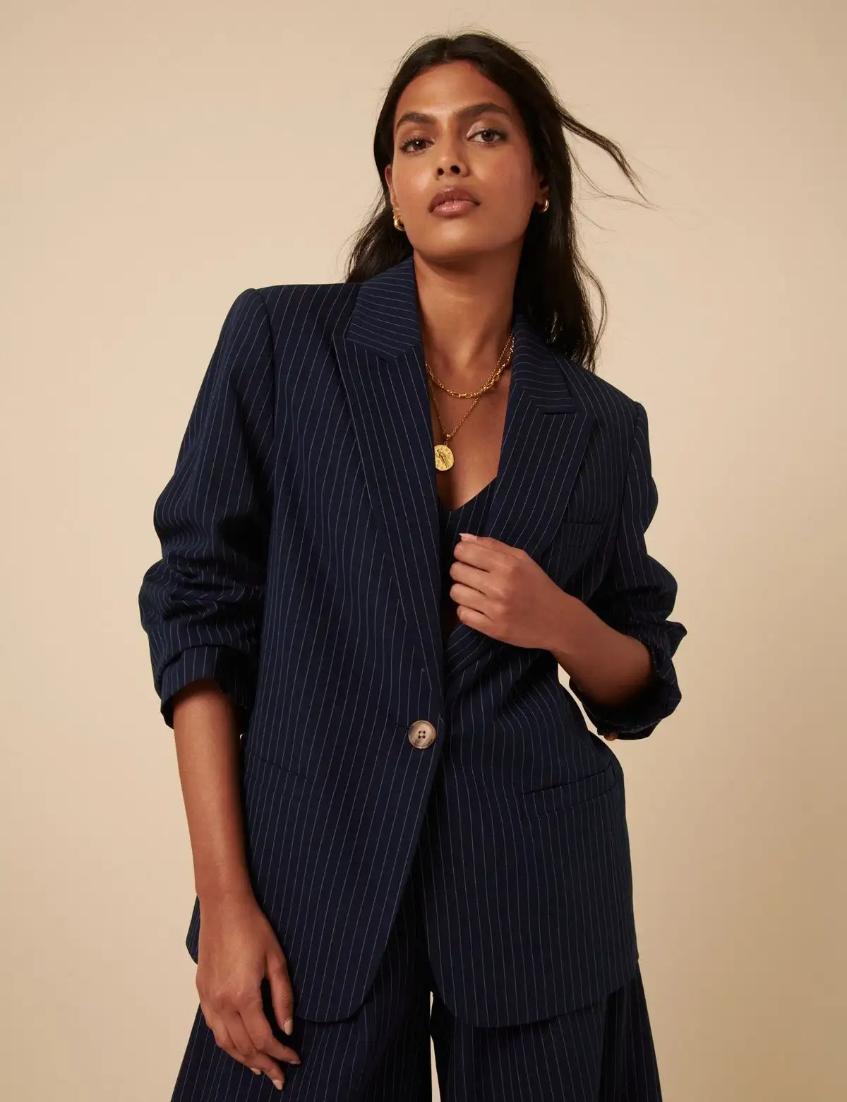 Stylish woman wearing a navy blue pinstripe blazer with matching trousers and a gold necklace, exuding modern professional elegance