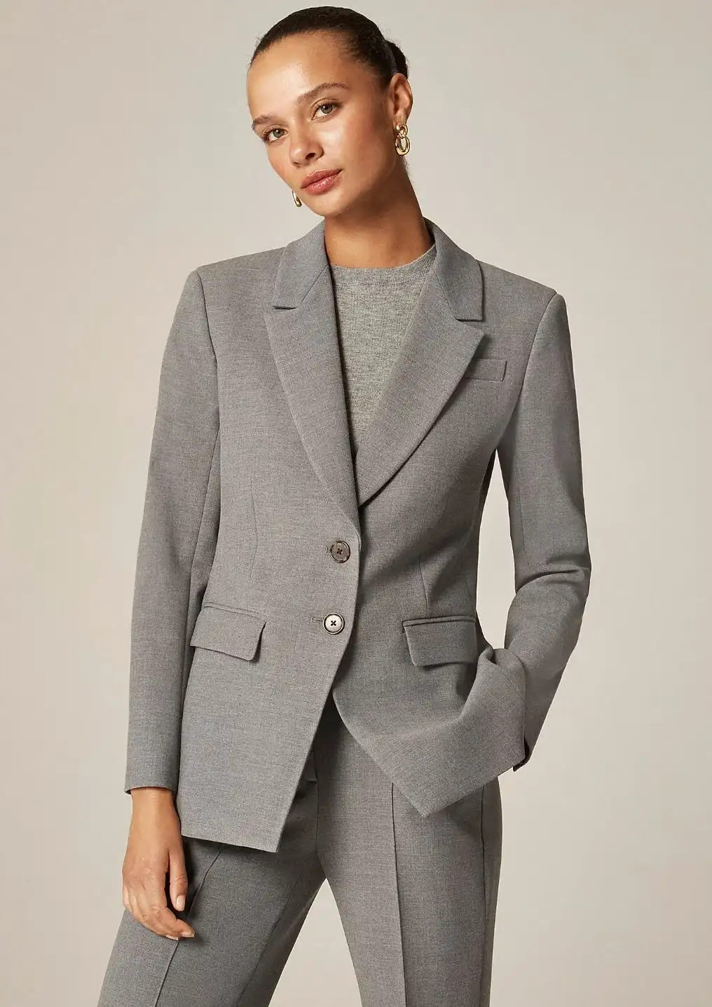 Professional woman wearing a tailored grey blazer with matching trousers and top, showcasing elegant business formal attire