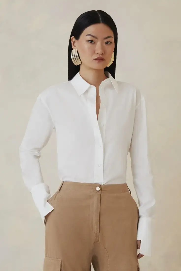 Female model wearing crisp white button-up blouse with pointed collar and long sleeves, tucked into high-waisted beige cargo trousers – bespoke women's stylish blouse