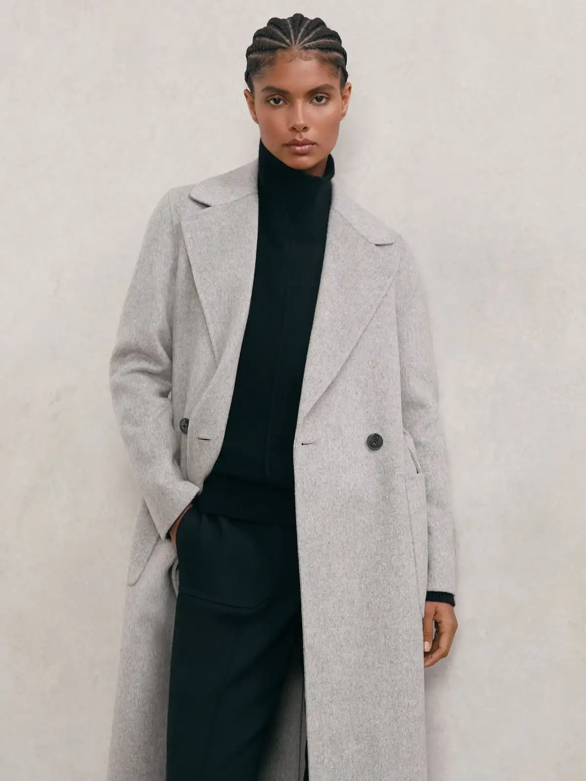 Woman wearing a long light gray overcoat over a dark turtleneck and trousers, embodying modern minimalist winter fashion