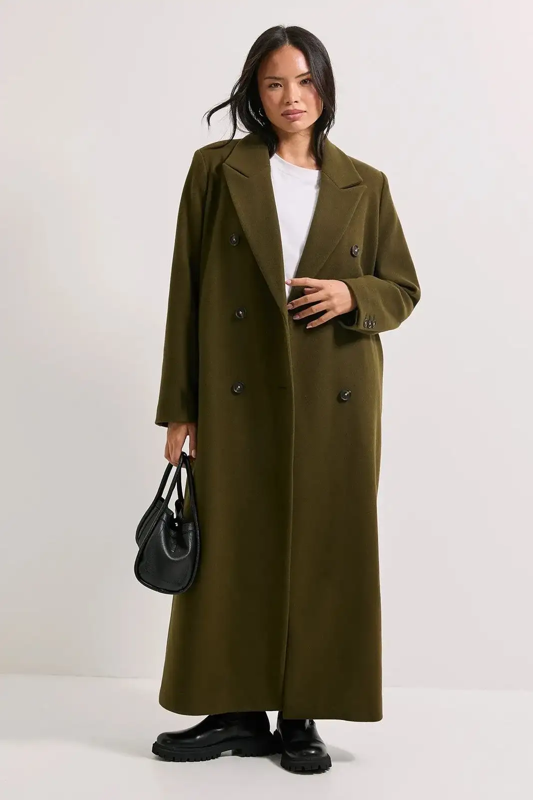 Woman wearing a long olive green double-breasted overcoat, carrying a black handbag, styled for sophisticated winter fashion