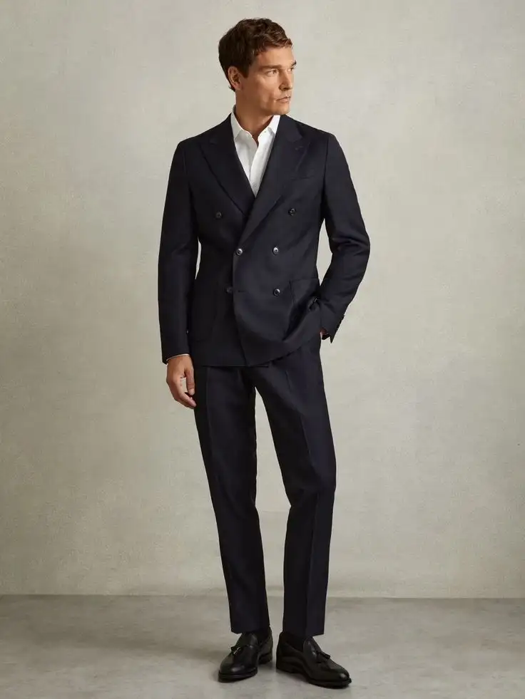Male model wearing navy double-breasted suit with peak lapels and matching trousers, paired with white dress shirt and dark dress shoes – Nordic Bespoke Tailor menswear