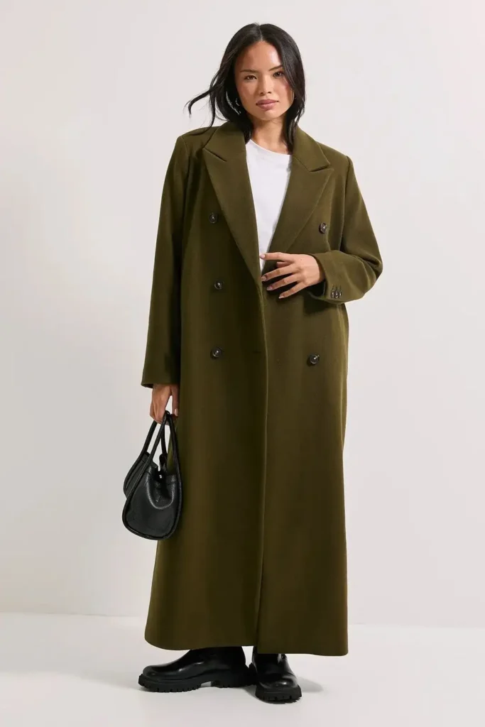 Woman wearing a long olive green double-breasted overcoat, carrying a black handbag, styled for sophisticated winter fashion