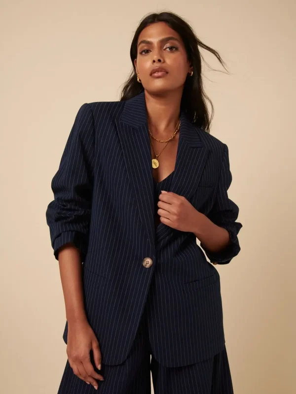 Stylish woman wearing a navy blue pinstripe blazer with matching trousers and a gold necklace, exuding modern professional elegance